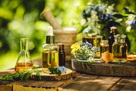 Mix of holistic flowers and herbs, salt, massage herb-infused essential oil in glass bottles. Aromatherapy, fragrance production. Herbal pure natural cosmetic ingredients on wooden background